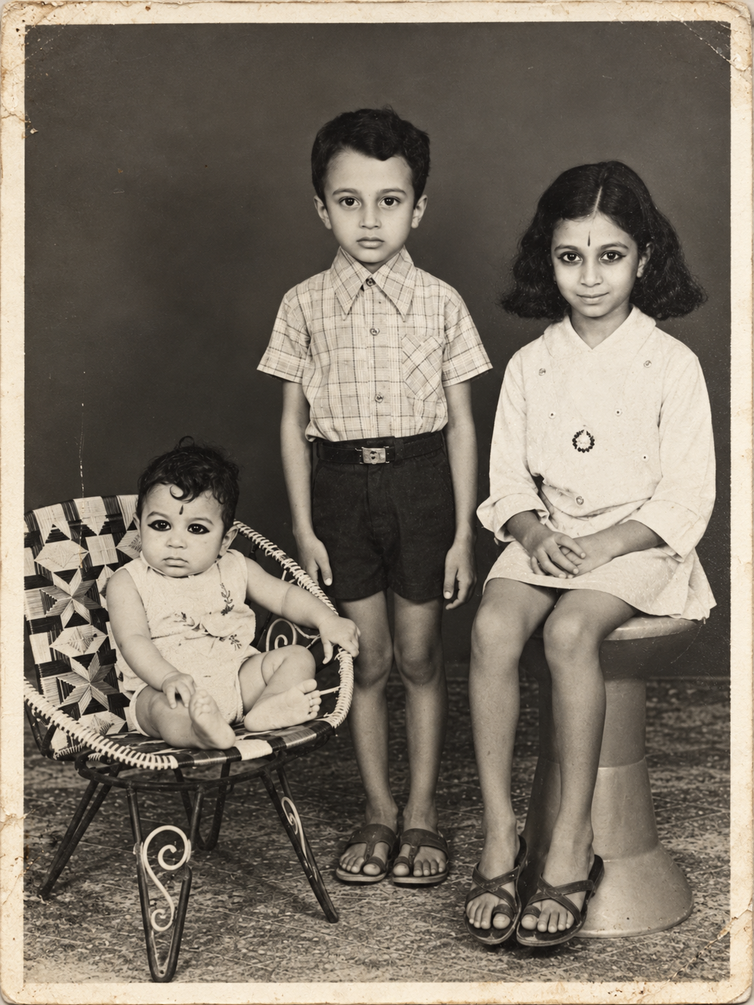 A family photograph of three children, with the youngest seated in a woven chair.