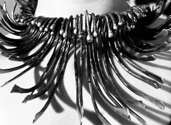 Close-up of The Plume necklace, with curved metal strands fanning from its collar.