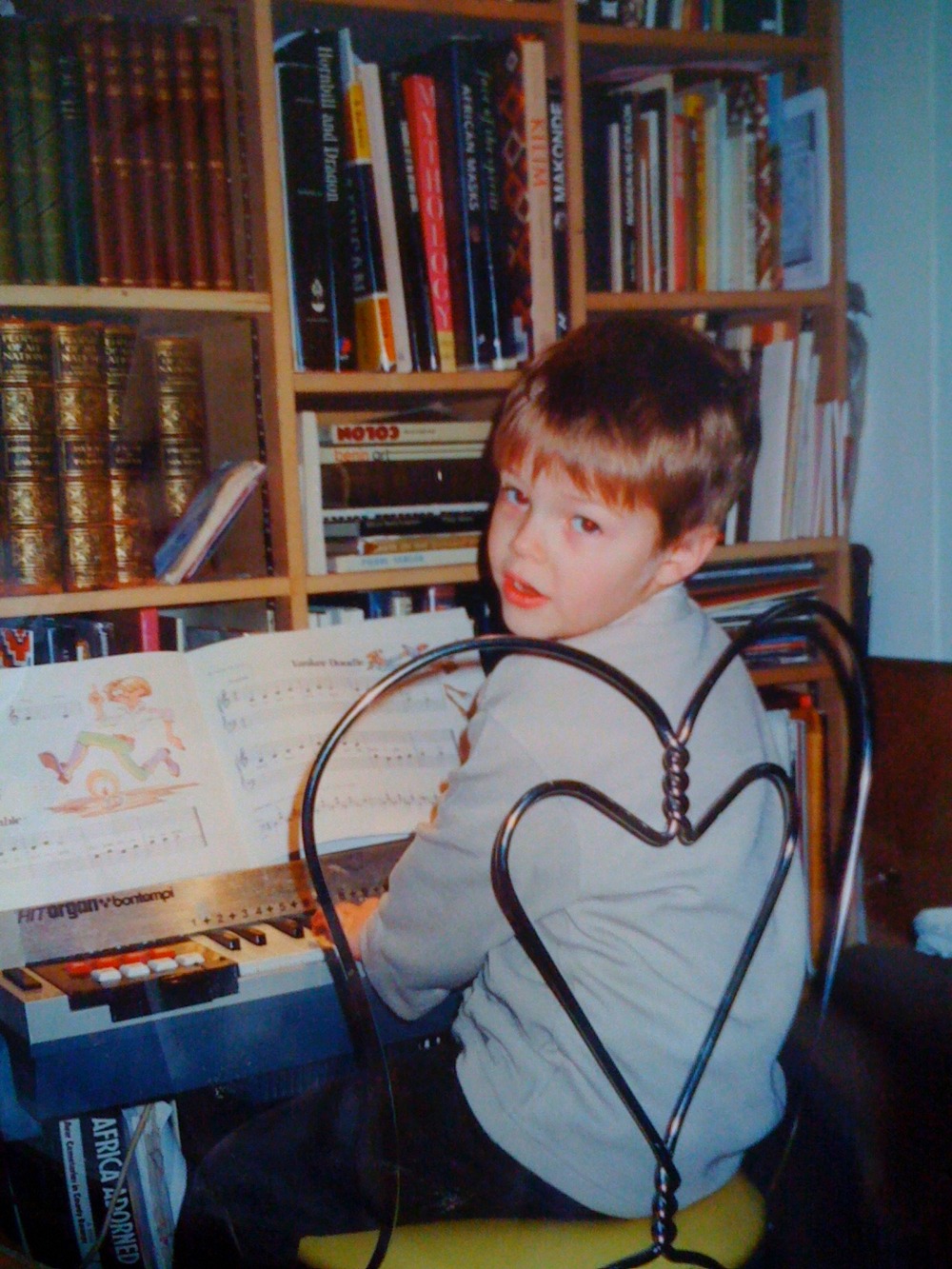 Milo as a child, seated at a keyboard in front of bookshelves.