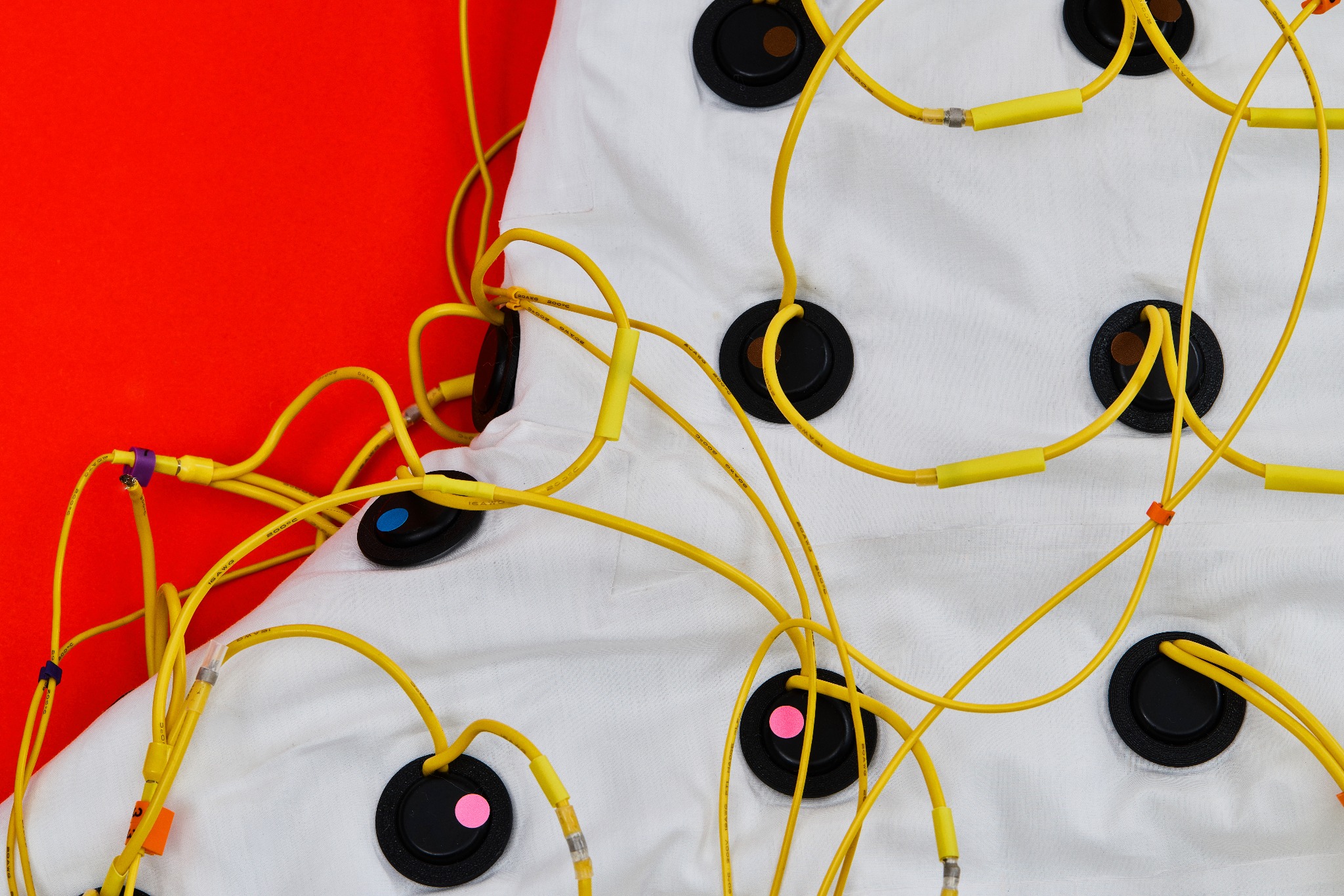 Close-up of black circular speakers and their yellow connecting wires fitted into the white jacket.