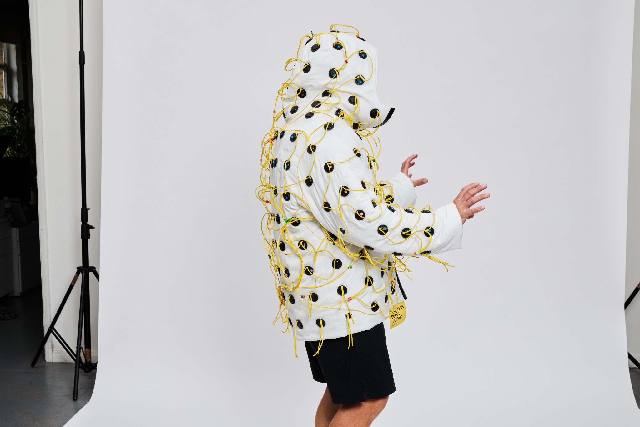 A person wearing the white Sonic Jacket with the hood raised in a photography studio.